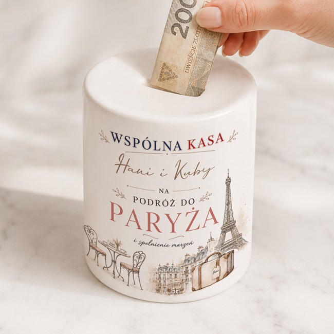 Biała ceramiczna skarbonka na prezent ślubny z imionami Pary Młodej, napisem na podróż do Paryża i grafiką Wieży Eiffla.