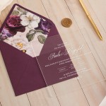 Ślubne zaproszenie w purpurowej kopercie z wklejką z nadrukiem kwiatowym. Przezroczysta tabliczka z białym tekstem.