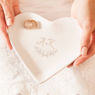 Podstawka ceramiczna w białym kolorze i w kształcie serca. Na powierzchni wzór z inicjałami Pary Młodej oraz dwoma gałązkami.